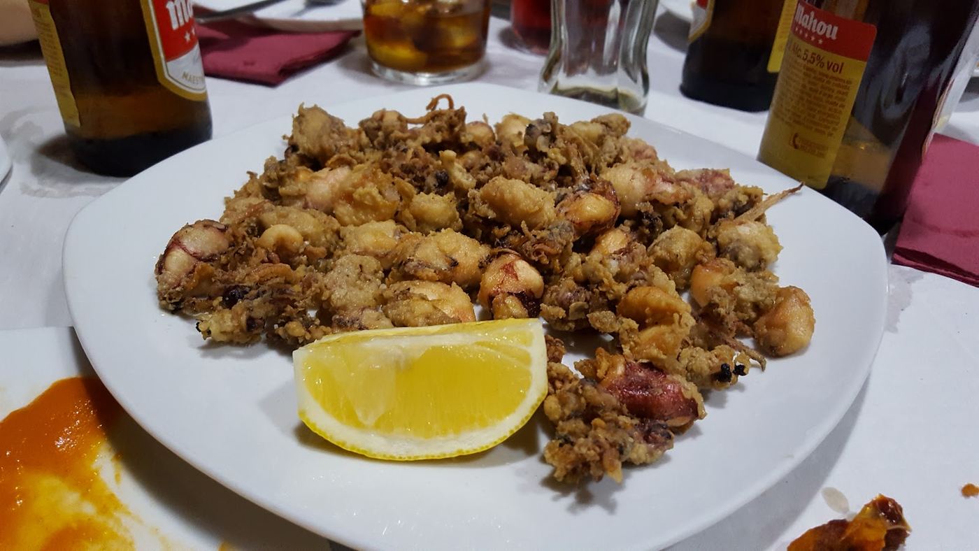 Ración de calamares fritos a la andaluza, dorados y crujientes, con un gajo de limón.